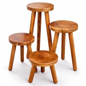 May include: Four wooden stools of varying heights. Each stool has a round seat and three angled legs. The wood has a warm, natural tone with visible grain. The stools are arranged together, showcasing their different sizes.