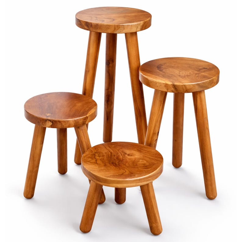 May include: Four wooden stools of varying heights. Each stool has a round seat and three angled legs. The wood has a warm, natural tone with visible grain. The stools are arranged together, showcasing their different sizes.