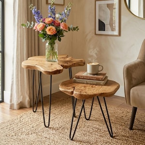 May include: Two nesting side tables with natural live-edge wood tops and black metal hairpin legs. The taller table holds a glass vase with orange and blue flowers. The shorter table holds a ceramic mug and two books titled Teak Wood Design.