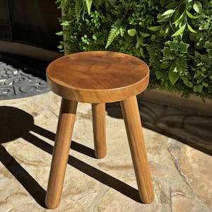 May include: A small, round wooden stool with three angled legs. The stool is made of light brown wood and has a smooth, polished finish. The stool is approximately 12 inches in diameter and 18 inches tall.