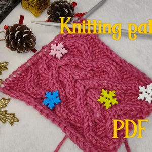 May include: A pink knitted fabric with a cable stitch pattern and snowflake buttons. The fabric is on a white surface with a gold snowflake and knitting needles. The text "Knitting patterns PDF file" is in the upper right corner of the image.