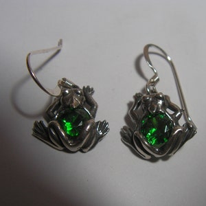 Puede incluir: Un par de pendientes de plata con forma de rana con detalles de piedras preciosas verdes.
