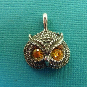 Op de afbeelding: Zilveren uil bedel met oranje edelsteen ogen. De uil is gedetailleerd met getextureerde veren en een kleine lus om aan een ketting of armband te bevestigen.