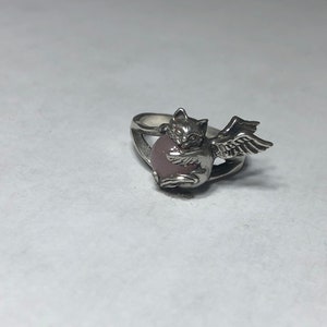 May include: A silver ring with a pink stone and a winged cat design.