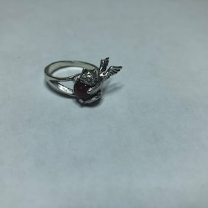 May include: Silver ring with a red gemstone and a winged angel design.