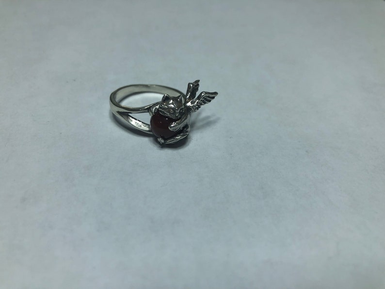 May include: Silver ring with a red gemstone and a winged angel design.