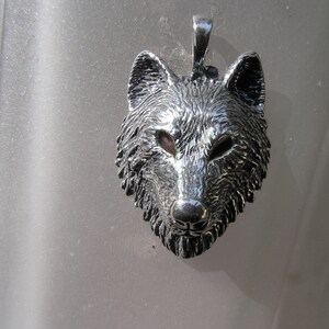 K&ouml;nnte beinhalten: Ein silberner Wolfskopf-Anh&auml;nger mit einem detaillierten, strukturierten Design. Der Anh&auml;nger ist eine realistische Darstellung eines Wolfskopfes mit einer spitzen Nase, spitzen Ohren und einem wilden Ausdruck.