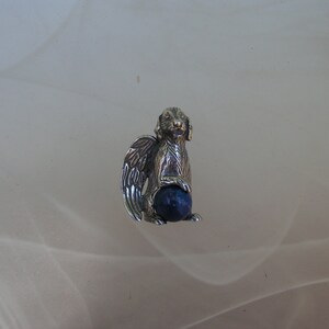 May include: A silver charm of a dog with wings holding a blue gemstone ball.