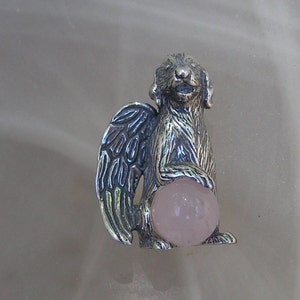 May include: Silver figurine of a dog with wings holding a pink rose quartz orb. The dog is standing on all four paws and has a sweet expression on its face.