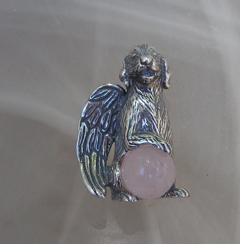 May include: Silver figurine of a dog with wings holding a pink rose quartz orb. The dog is standing on all four paws and has a sweet expression on its face.