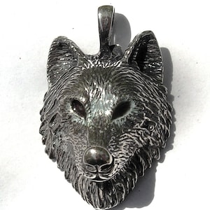 K&ouml;nnte beinhalten: Ein silberner Wolfskopf-Anh&auml;nger mit detailliertem Design. Der Anh&auml;nger ist eine realistische Darstellung eines Wolfskopfes mit Fell und Gesichtsz&uuml;gen.