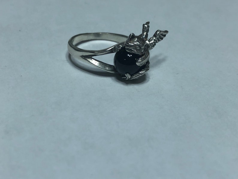 May include: A silver ring with a black gemstone and a winged creature design.