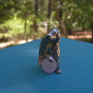 May include: A silver figurine of a dog holding a pink ball. The dog is standing on a blue surface.