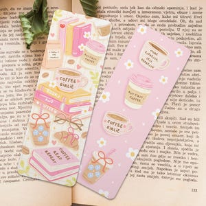 以下が含まれることがあります： コーヒーと本のイラストが描かれた2つのピンクのブックマーク。1つは「Coffee Girlie」、もう1つは「Read, Repeat」と書かれています。ニュートラルな色合いの毛布がかけられた開いた本の上に置かれています。