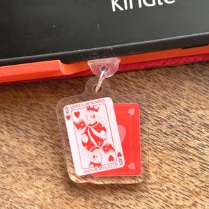 May include: A clear acrylic keychain featuring a red and white Queen of Books playing card design. The keychain also includes a red playing card with a heart symbol. The word "kindle" is visible in the background.