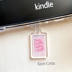 May include: A clear acrylic keychain in the shape of a library card. The card has pink lines and text that reads "Sorry, I'm fully booked tonight!" The keychain is hanging in front of a Kindle e-reader.