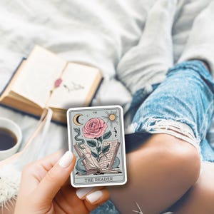 May include: A tarot card with a blue background and a pink rose with a snake wrapped around it. The card reads "The Reader" at the bottom.