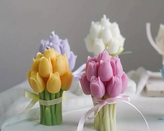 May include: A set of three floral bouquet candles. The candles are shaped like tulips and are tied with a ribbon. The candles are in shades of yellow, pink, and white.