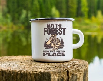 May include: White enamel camping mug with a black rim and handle. The mug features a graphic of a skeleton hiker with a backpack and the text "May the Forest be my final resting place."