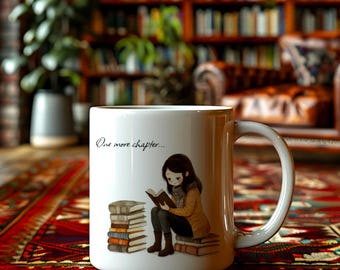 May include: White ceramic mug with a wraparound illustration of a person reading a book, with the text "One more chapter...". The illustration features a stack of books and a person wearing a scarf and jacket. The mug has a white handle.