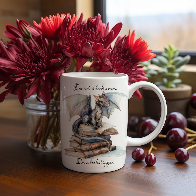 May include: White ceramic mug with a blue and gray dragon sitting on a stack of books. The mug has the text "I'm not a bookworm, I'm a bookdragon." printed on it.