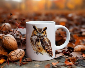 May include: White ceramic mug with a brown and yellow owl illustration. The owl is looking directly at the viewer. The mug is sitting on a bed of brown leaves.