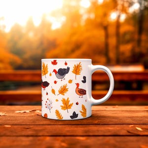 May include: White ceramic mug featuring a fall-themed design. The mug is adorned with illustrations of turkeys, autumn leaves, and berries in shades of red, orange, black, and yellow. The mug has a curved handle and is set on a wooden surface.