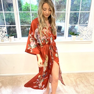 May include: A long, red silk robe with a floral and bird print. The robe has a tie belt and a side slit.