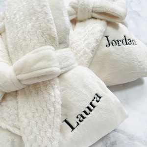 May include: Two white plush bathrobes with black embroidered names, "Laura" and "Jordan".