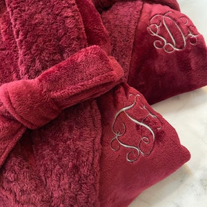 May include: Two plush burgundy robes with embroidered initials. The robes have a tie belt and a hood.