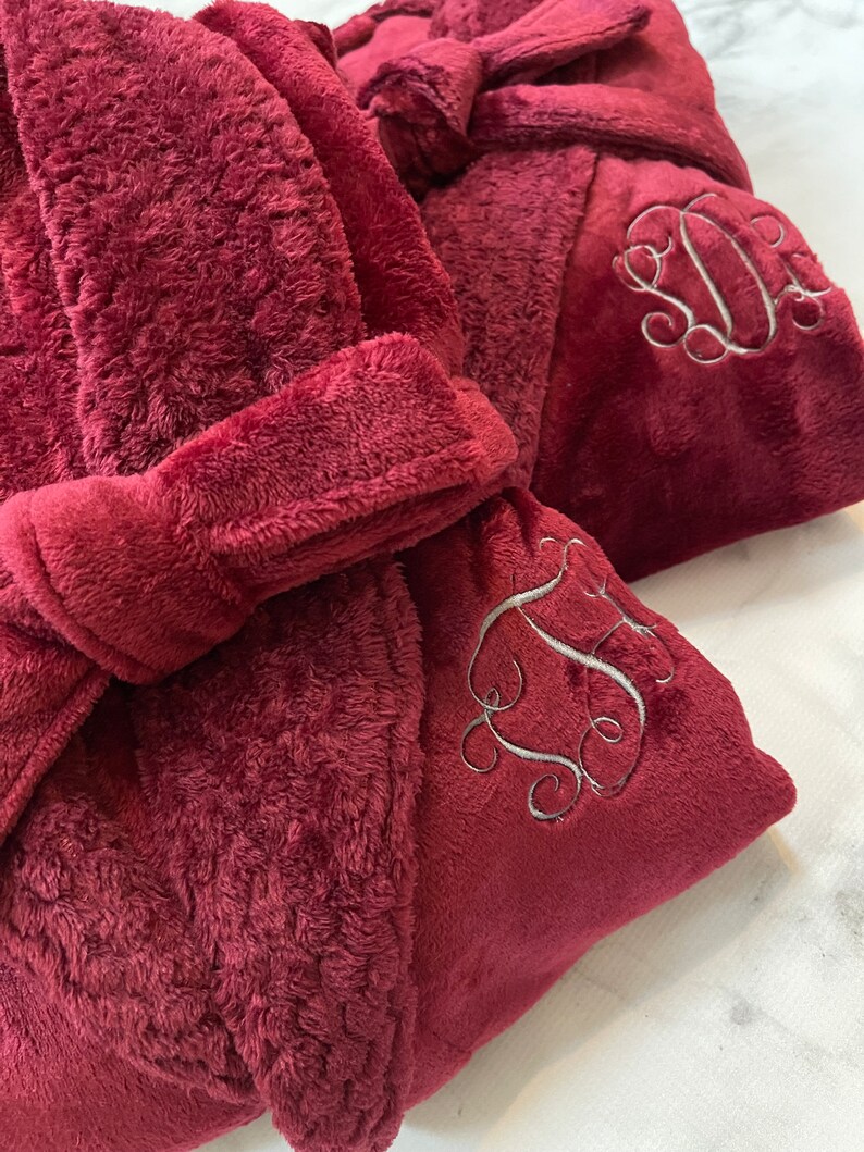 May include: Two plush burgundy robes with embroidered initials. The robes have a tie belt and a hood.