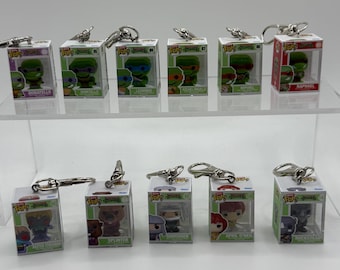 Pode incluir: Coleção de chaveiros Funko Pop! das Tartarugas Ninja. Cada chaveiro apresenta um personagem diferente em uma caixa transparente. Os personagens incluem Donatello, Leonardo, Raphael e outros. Os chaveiros têm fechos de metal prateado.