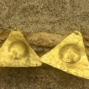 May include: A pair of gold triangle earrings with a hammered texture and a circular indentation in the centre of each triangle.