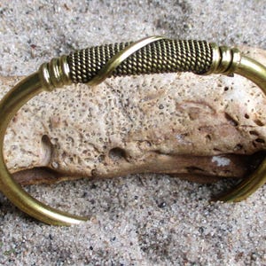 May include: A gold-toned metal cuff bracelet featuring a central section of tightly coiled wire wrapped with a smooth, diagonal metal band. The bracelet has a polished finish and a C-shaped open design with rounded ends, showcasing a metallic texture.