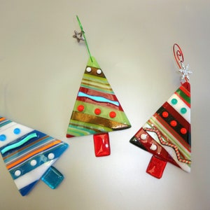 May include: Three colorful glass Christmas tree ornaments. Each tree has a unique design with stripes, dots, and a red base. One is blue, one is green, and one is red, with silver wire hangers and star or snowflake toppers.