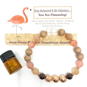May include: An illustration of a pink flamingo with the text "Stay Balanced & Be Fabulous... You Are Flamazing!" A bracelet with brown, pink, and gold beads. The bracelet is made with cherry quartz, rock crystal, and garnet. The text "Juna Gems Holistic Gemstone Jewelry" is visible on a gold glitter background.