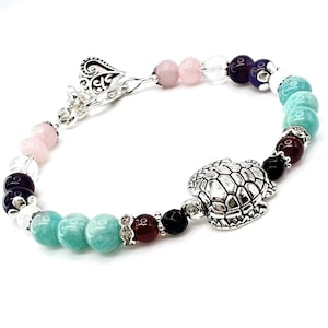 May include: A silver charm bracelet with a turtle charm. The bracelet features pink, clear, purple, green, red, and black beads.