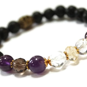 Puede incluir: Pulsera elástica con una combinación de roca volcánica negra, amatista, cuarzo ahumado, cuarzo transparente y cuentas doradas. Las cuentas de la pulsera miden aproximadamente 8 mm. Un accesorio elegante y versátil.