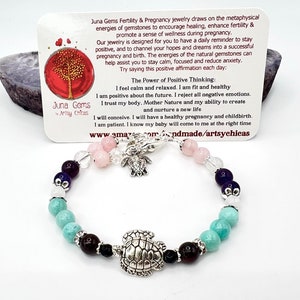 May include: A gemstone bracelet with a silver turtle charm and various colorful beads, including turquoise, rose quartz, and amethyst. The bracelet is displayed with a card that has text about fertility and pregnancy.