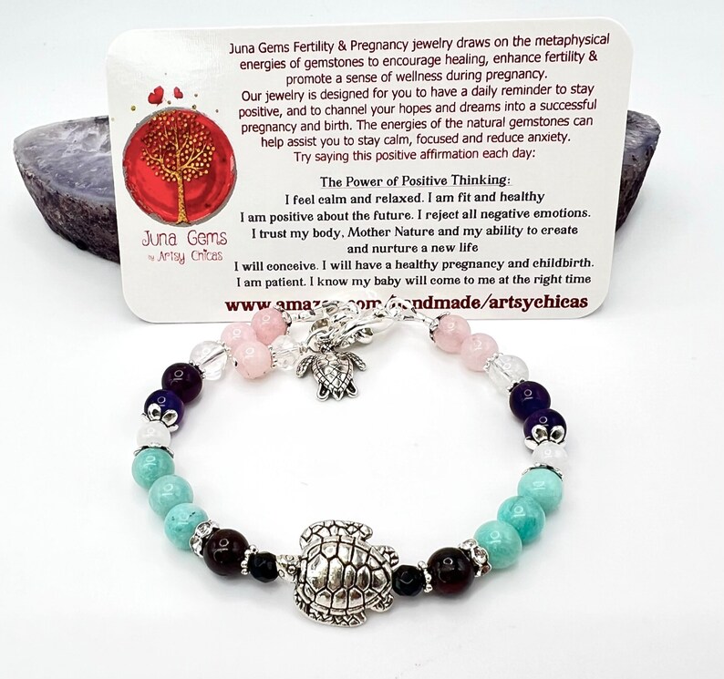 May include: A gemstone bracelet with a silver turtle charm and various colorful beads, including turquoise, rose quartz, and amethyst. The bracelet is displayed with a card that has text about fertility and pregnancy.