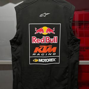 May include: A black sleeveless vest featuring a high collar and a white Alpinestars logo on the upper back. A large rectangular graphic on the back displays the Red Bull logo, the orange KTM Racing logo, and the Motorex logo in white and yellow.