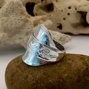 May include: A silver ring crafted from a recycled spoon, featuring a rose design. The ring is wide and has a distinctive, angled shape.