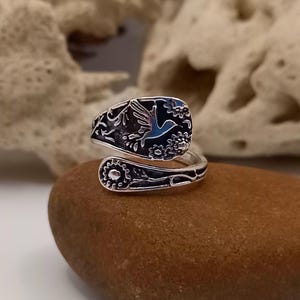 May include: Silver ring featuring a bird and floral design. The ring is crafted from a spoon and is adjustable.