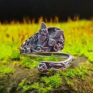 May include: A silver ring featuring a butterfly and floral design. The ring is crafted from a spoon and is adjustable.