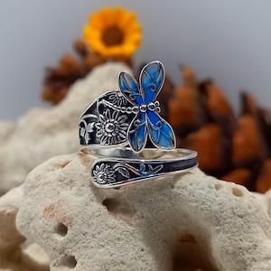 May include: A silver ring featuring a blue butterfly design with floral accents. The butterfly has a black outline and blue enamel wings.