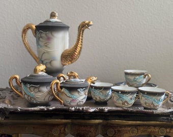 May include: A vintage tea set with a dragon design. The set includes a teapot, creamer, sugar bowl, and six teacups. The teapot has a gold dragon handle and spout. The teacups and other pieces have a black and white dragon design with gold accents.