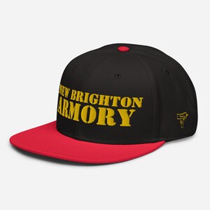 May include: A black and red baseball cap with the words "NEW BRIGHTON ARMORY" embroidered in gold. The cap has a flat brim and a small gold graphic of a gun on the side.
