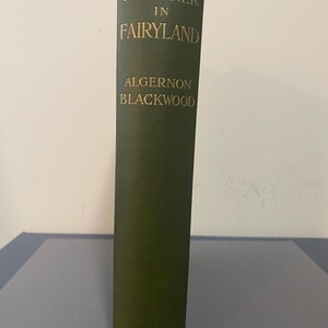 May include: A vintage hardcover book titled "A Prisoner in Fairyland" by Algernon Blackwood. The book has a dark green cover with gold lettering. The publisher's name, Macmillan & Co, is at the bottom.