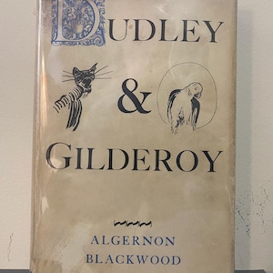 May include: A vintage book titled "Dudley & Gilderoy" by Algernon Blackwood. The cover features illustrations of a cat and a parrot, with the title in large, dark blue letters. The book is wrapped in clear plastic.