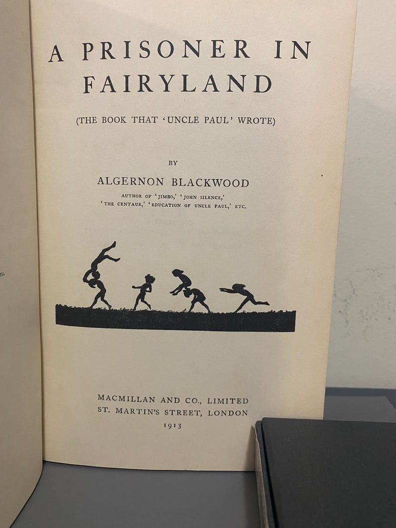 May include: A vintage book titled "A Prisoner in Fairyland" by Algernon Blackwood. The cover features a silhouette of figures in motion. Published in 1913 by Macmillan and Co., Limited, St. Martin's Street, London.